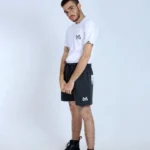 Joven modelo con camiseta blanca Aypanda de diseño minimalista y shorts acolchados negros con logo, mostrando estilo casual y cómodo de verano.