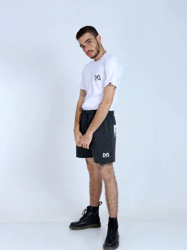Joven modelo con camiseta blanca Aypanda de diseño minimalista y shorts acolchados negros con logo, mostrando estilo casual y cómodo de verano.