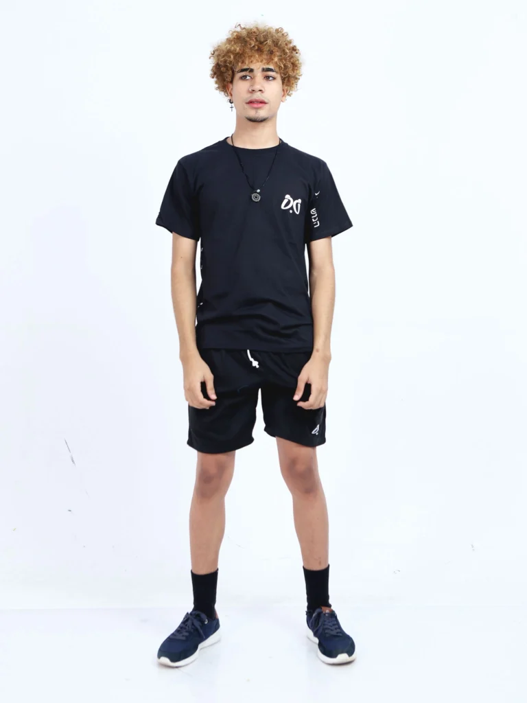 Joven modelo con cabello rizado, vistiendo conjunto Aypanda de camiseta negra oversized y shorts negros deportivos con logo blanco, mostrando estilo casual y libertad.