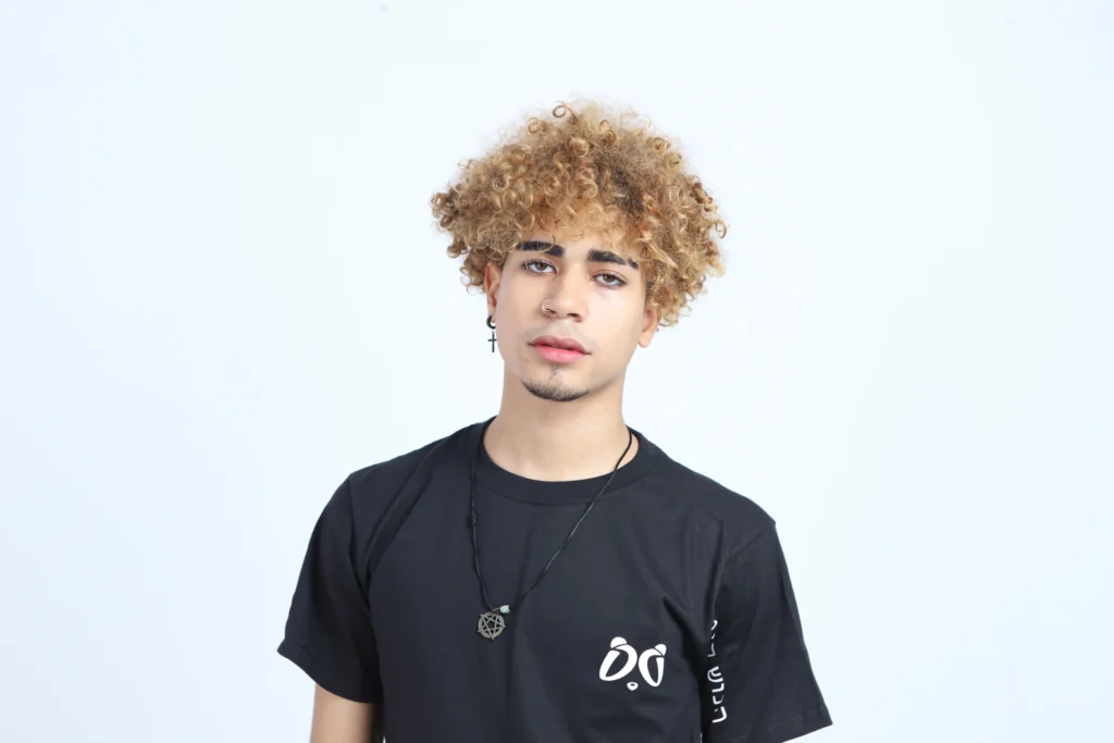Retrato de joven modelo con cabello rizado rubio, usando camiseta negra Aypanda con logo blanco, transmitiendo la esencia auténtica y juvenil de la marca.