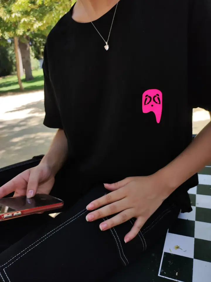 Persona usando camiseta negra Fruit of the Forest de Aypanda con logo rosa en el pecho, sentada al aire libre.