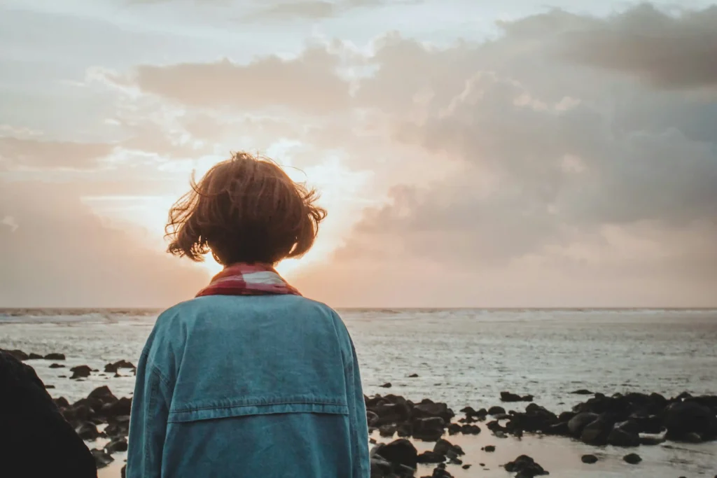 Mujer de espaldas mirando un atardecer sobre el mar, simbolizando el crecimiento personal y un nuevo comienzo.